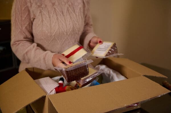 Someone in a sweater opens a Care Package Quarterly box filled with diverse items like packaged food and wrapped gifts.